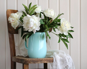 white peonies in a jug on an old chair.