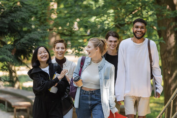 Smiling asian student walking near multicultural friends in summer park.