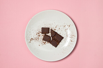 Slices of chocolate sprinkled with cocoa on a white plate on a pink background. Sweet treat. Dessert serving.
