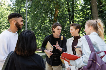 Students with backpacks talking near multicultural friends in park.