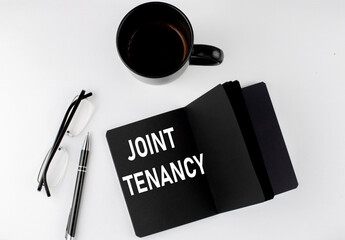 Naklejka premium JOINT TENANCY written text in small black notebook with coffee , pen and glasess on white background. Black-white style