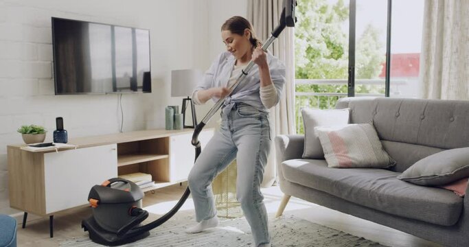 Young woman cleaning and dancing with vacuum cleaner in her apartment. Cheerful female listening to music while doing housework at home. Energetic female doing chores spring cleaning a lounge