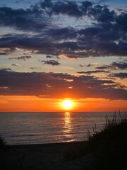 Sunset into the ocean. Blue clouds contrast with orange sunrays.