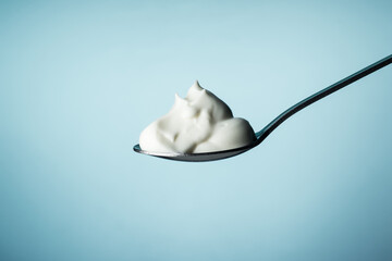 Sour cream in a spoon on a blue background - obrazy, fototapety, plakaty
