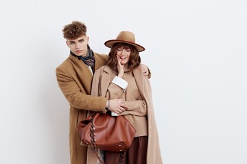 a beautiful, loving couple of a man and a woman stand on a white background in stylish autumn clothes, gently embracing and the woman joyfully holds her hand near her face