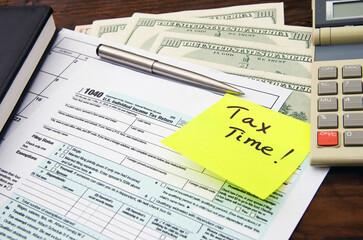 1040 US individual tax form, calculator, dollars, pen, paper note and yellow sticker