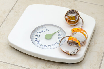 Floor scales and measuring tape on the bathroom floor, tiled with marble ceramic tiles