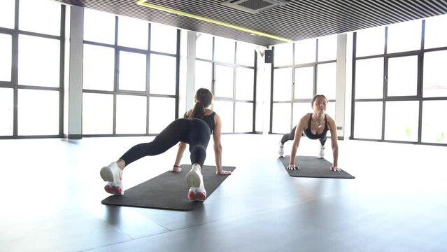 Two sporty women doing exercise abdominal crunches, pumping a press on floor in 