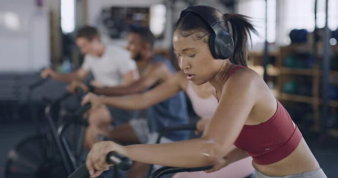 Fit people using air bikes for cardio exercise in gym. Diverse group of athletic, healthy men and women listening to music on earphones or headphones. A sweaty workout and training class with friends