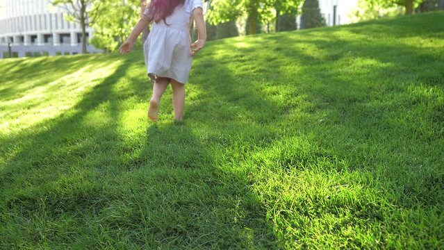 Close-up of a little girl in a dress jumping on a beautiful lawn with bare feet at sunset.Happy childhood in the fresh air,bright emotions.A child jumps on the grass. A child is having fun in the park