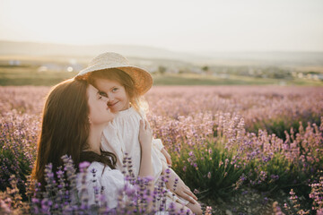 Happy mother and daughter wearing white vintage dresses having fun in lavender field at sunset.