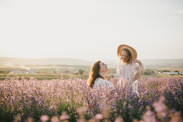 Happy mother and daughter wearing white vintage dresses having fun in lavender field at sunset.