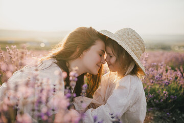 Happy mother and daughter wearing white vintage dresses having fun in lavender field at sunset.