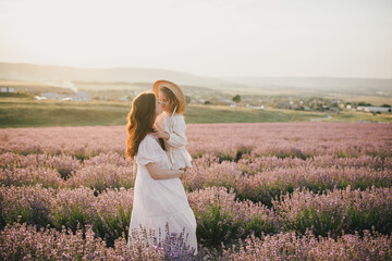 Fototapeta na wymiar Happy mother and daughter wearing white vintage dresses having fun in lavender field at sunset.