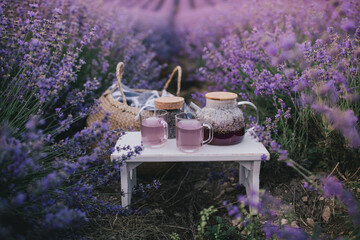 Herbal lavender tea in mugs and tea pot on wooden tray on purple flower field.