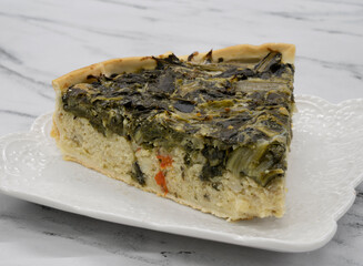 Tart. Closeup view of a slice of chard pie in a white dish on the marble table.