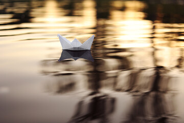 A paper boat is floating on the waves in the water at a beautiful sunset. Origami ship Sailing. The...