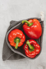 Fresh ripe sweet red bell pepper in eco-friendly reusable produce bag on gray background. Healthy grocery, vegan food and ingredients for cooking concept