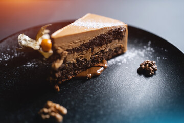closeup of chocolate nut cake with walnut and physalis on black plate
