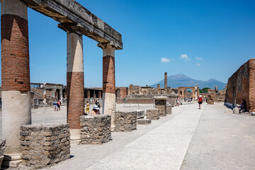 Tourists walk among the excavations of Pompeii, Vesuvius is visible in the distance. Naples Italy