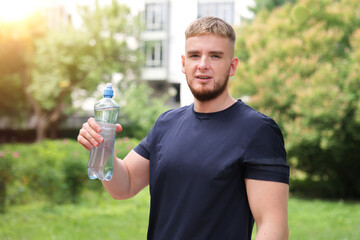 Portrait of handsome guy, young happy thirsty man runner is drinking pure fresh water from plastic...