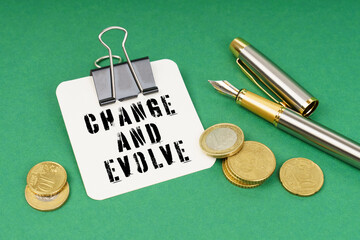 On a green surface, a pen, coins and a notepad with the inscription - Change and evolve