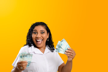 smiling woman holding 100 reais notes in her hands, Brazilian money, isolated on orange background