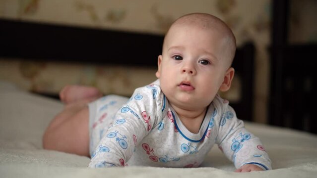 Newborn Active Baby Cute Smiling Teethless Face Portrait Early Days On Stomach Developing Neck Control. 5 Months Child On White Bed Looking on Camera. Infant, Childbirth, Parenthood, Beginning Concept