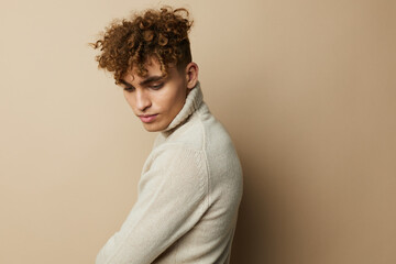 Fototapeta na wymiar portrait of a handsome man, with curly hair, standing on a beige background in a light turtleneck, looking down. A photo with an empty space for inserting an advertising layout