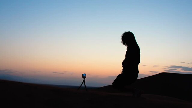 Young caucasian woman check smartphone on tripod take selfie on desert with . Travel photographer on field concept.