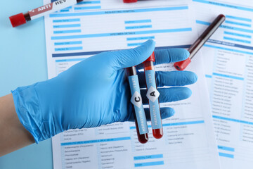 Scientist holding tubes with blood samples for hepatitis virus test near laboratory form, closeup