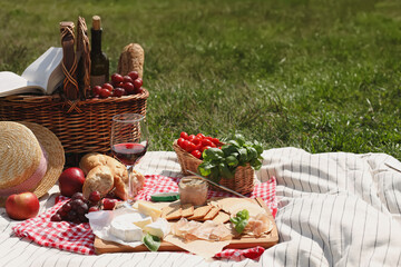 Blanket with picnic basket and different products on green grass