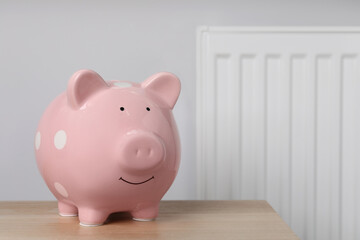 Piggy bank on wooden table near heating radiator, space for text