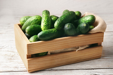 Crate full of fresh ripe cucumbers on white wooden table
