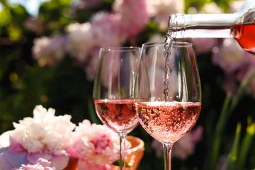 Gordijnen Pouring rose wine into glass in garden, closeup © New Africa