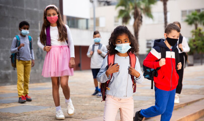 Obraz premium Schoolchildren in masks walking together on the street from school at day
