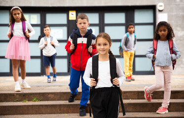 Fototapeta premium Portrait of smiling schoolgirl standing on the street, kids on background