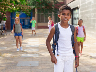 Fototapeta premium Focused african american preteen boy carrying backpack on his shoulders, walking outdoors on sunny autumn day, going to school