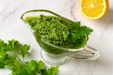 Chimichurri dipping sauce in a gravy boat on a table. Green sauce from fresh parsley, garlic cloves, olive oil and lemon juice. Salsa verde with fresh herb and spices. Healthy condiment.