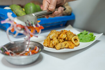 Cook plating ceviche in a dish with breaded meat and fish