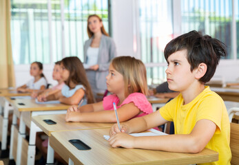 Sad bored schoolboy sitting in classroom during lesson in elementary school