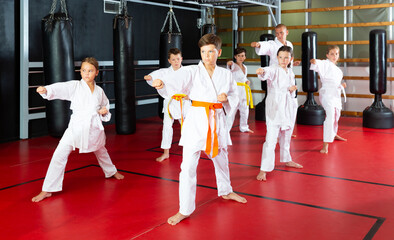 Young boys and girls in kimono doing kata moves with their trainer in gym.