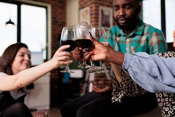 Happy smiling diverse people clinking glasses while celebrating birthday event. Joyful multiracial group of best friends toasting wineglasses while enjoying wine party at home.