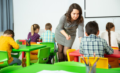 Positive boys and girls studying and female teacher helping in classroom. High quality photo