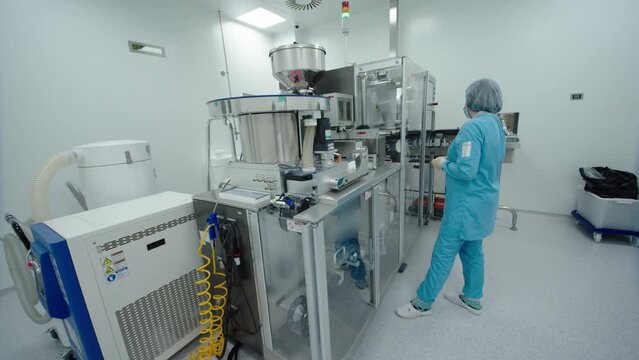 Pharmaceutical employee control the automated machinery work. woman in protective mask and medical uniform is monitoring the working process of drug producing equipment.