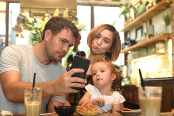 Young parents with daughter make selfie in a cafe