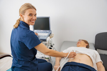 Smiling doctor ultrasound examine senior patient abdomen at hospital and looking camera