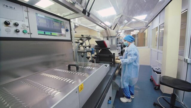 Pharmaceutical worker examines and controls the production line. woman in protective mask and medical uniform monitors the quality of fabricated medicine on the manufacturing equipment.