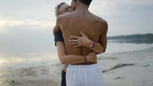 Interracial couple with age differences embrace and kissing on beach at sunset - push back slow motion