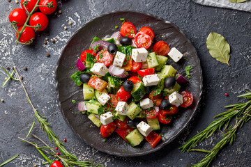 Greek salad with feta and vegetables on dark plate on stone table top view
